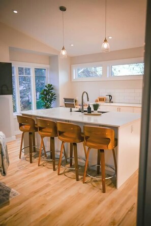 A modern kitchen with a large island, bar stools, pendant lighting, and a view of the outdoors. - Courtenay Luxe Suite (Courtenay)