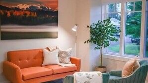 Un salon comprenant un canapé, des fauteuils, une table basse, un tableau, une plante et une fenêtre donnant sur un beau paysage.