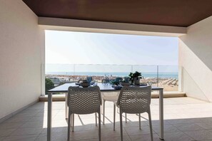 Ein Balkon mit Tisch und zwei Stühlen, mit Blick auf Strand und Stadtbild.