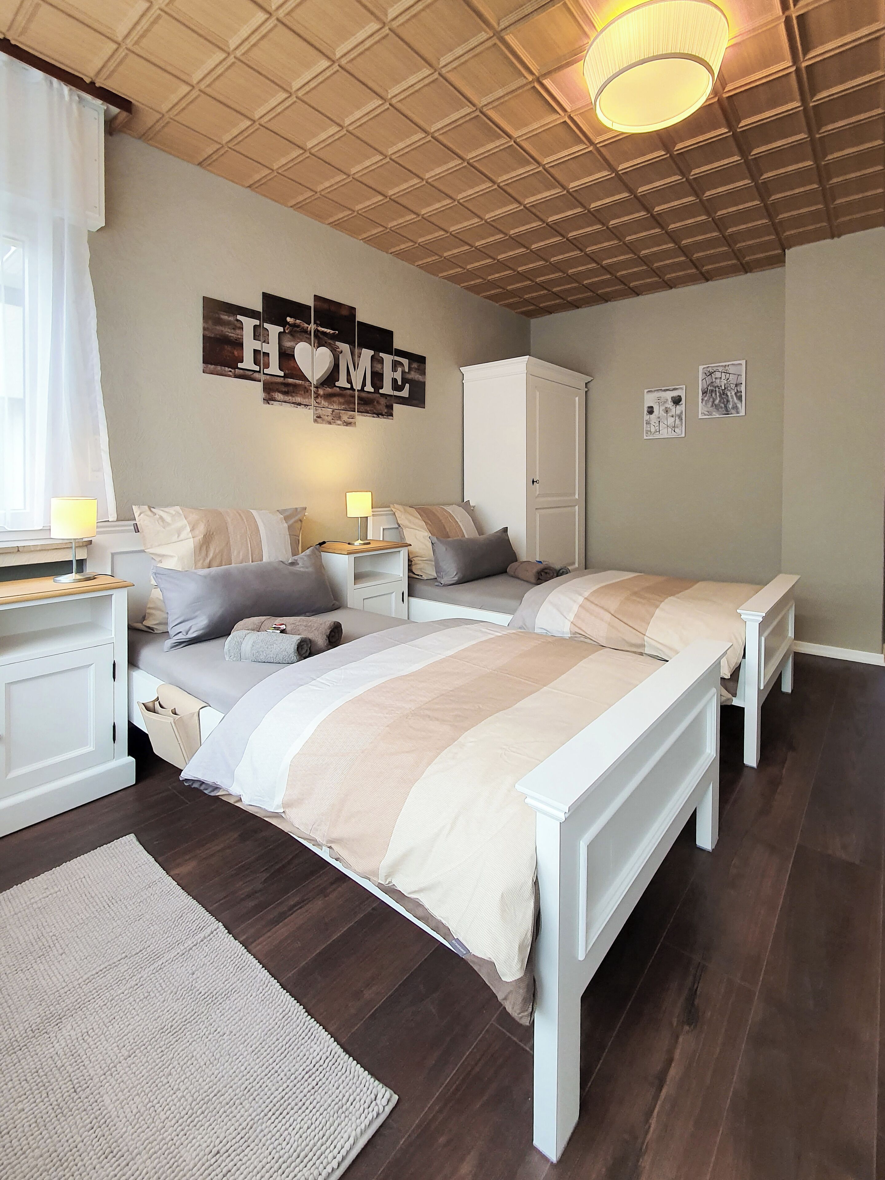 Een slaapkamer met twee bedden, een garderobe, een nachtkastje en een muur met decoratie met het woord 'HOME'.