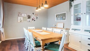 A dining area with a wooden table, white chairs with green cushions, and a white cabinet with glass doors. - Friendly Home - Villa Verde - near Phantasialand/Cologne/Bonn (Bornheim)