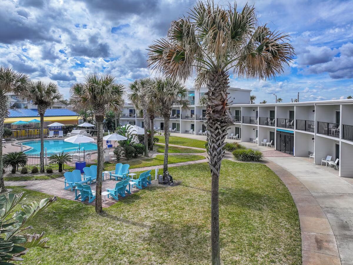 Een hotel met een zwembad, terras en palmbomen.