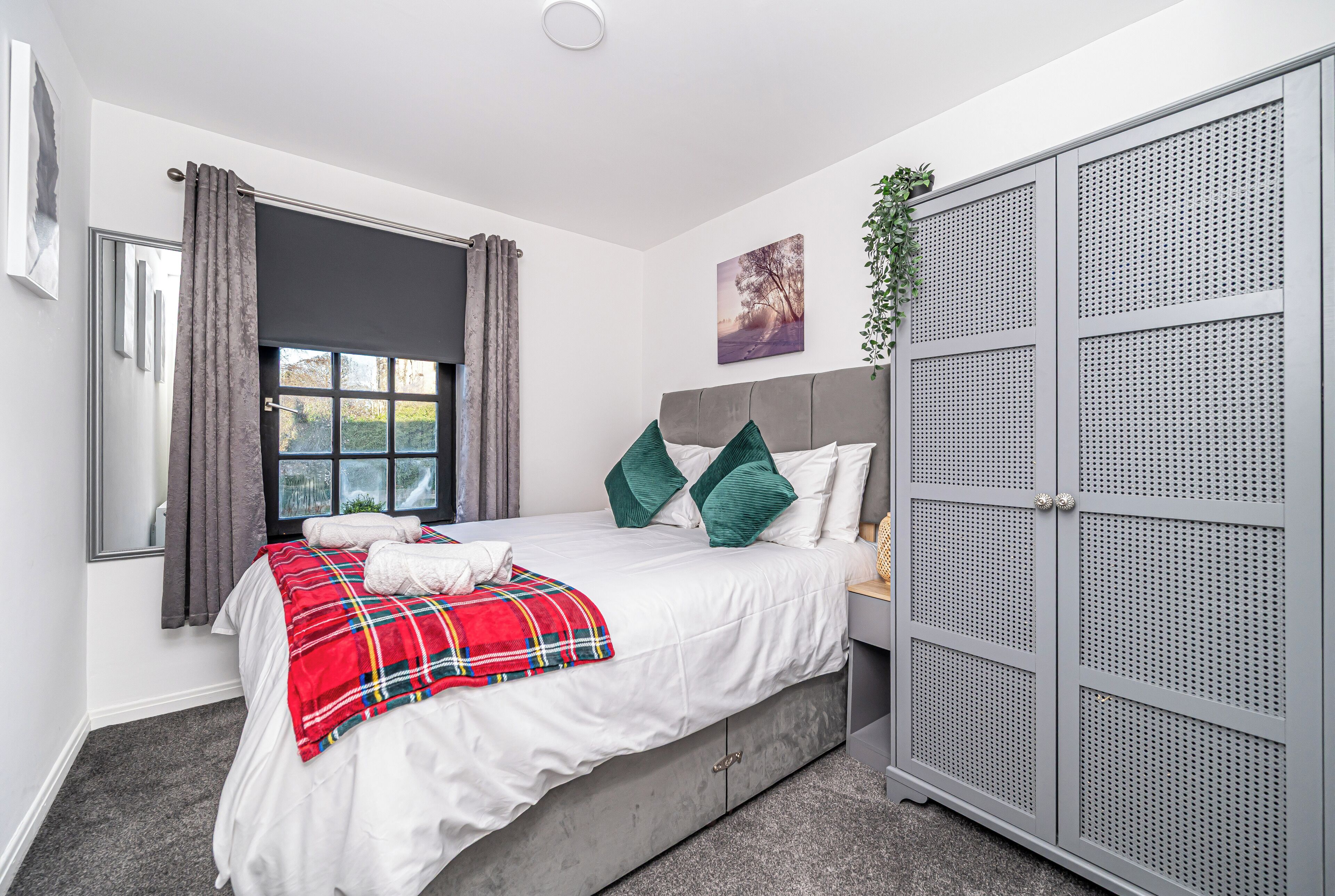 A bedroom with a bed, grey wardrobe, and a window with curtains.