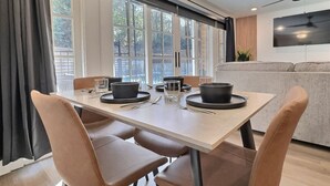 A modern dining area with a table set for two, large windows, and a grey sofa in the background. - Lavish Suite w/ Pool & Extra Large Balcony (Birmingham)
