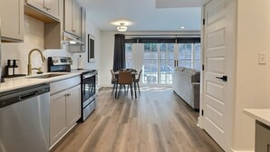 A modern kitchen with white cabinets, a dining area with a table and chairs, and a large sliding glass door leading to a balcony. - Lavish Suite w/ Pool & Extra Large Balcony (Birmingham)
