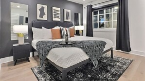 A modern bedroom with a bed, bedside tables, a ceiling fan, and artwork on the wall. - Lavish Suite w/ Pool & Extra Large Balcony (Birmingham)