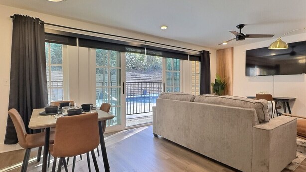 A modern living room with a sofa, dining table, chairs, and a TV. - Lavish Suite w/ Pool & Extra Large Balcony (Birmingham)
