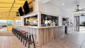 A bar area with stools, a counter, and a ceiling fan. - Explore Local Gems from a Relaxing Beachfront Room with Outdoor Swimming Pool (Neptune Beach)