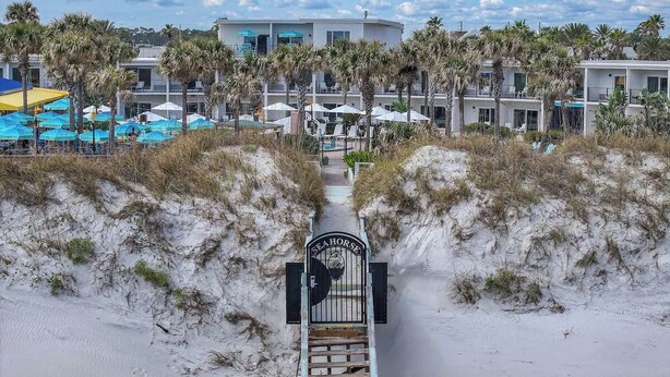 A beachside hotel entrance with a gate labeled "SEA HORSE" leading to a pathway flanked by sand dunes and palm trees. - Explore Local Gems from a Relaxing Beachfront Room with Outdoor Swimming Pool (Neptune Beach)