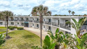 Un hotel de varios pisos con balcones, un patio ajardinado y plantas tropicales.