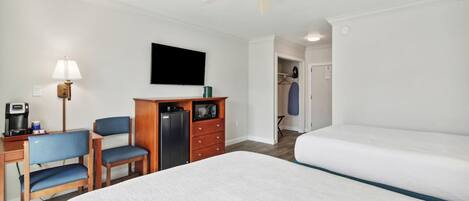Ein Hotelzimmer mit Bett, Schreibtisch mit Computer, Stuhl, Kleiderschrank und Deckenventilator.