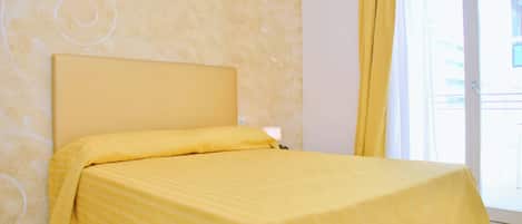 Una cama con cabecera en una habitación con pared estampada y ventana con cortinas.