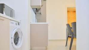 A compact kitchen with a washing machine, a small refrigerator, and two chairs. - Sunny and Bright Beautiful Apartment (San Michele al Tagliamento)