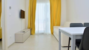 A small, well-lit room with a white sofa, a small table, and a TV mounted on the wall. - Sunny and Bright Beautiful Apartment (San Michele al Tagliamento)
