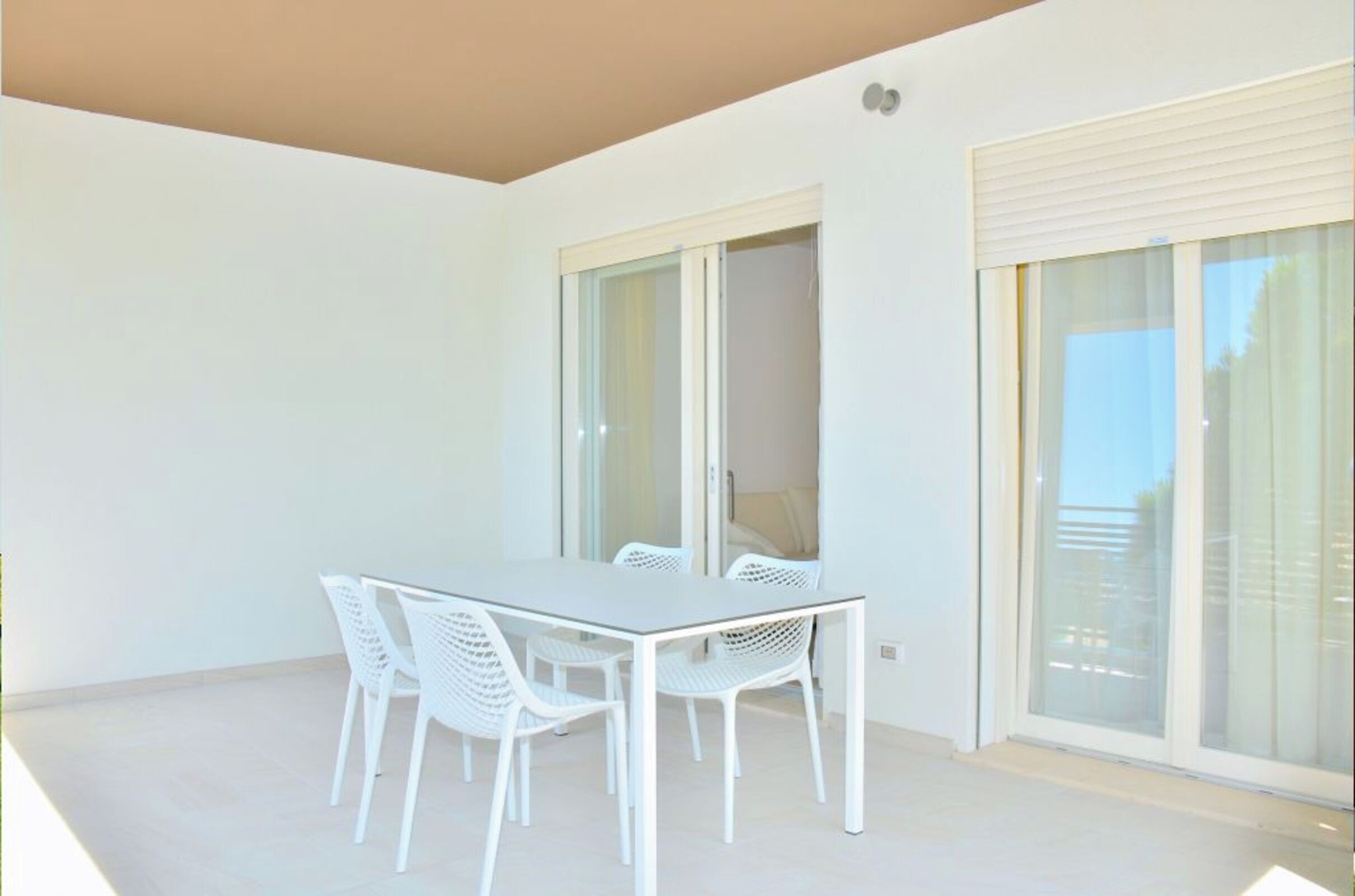 A balcony with a white table and chairs, a sliding glass door, and a view of the outside.
