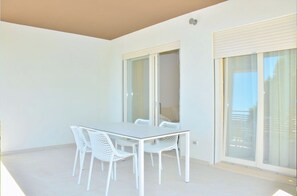 Ein Balkon mit weißem Tisch und Stühlen, einer Schiebeglastür und Blick ins Freie.