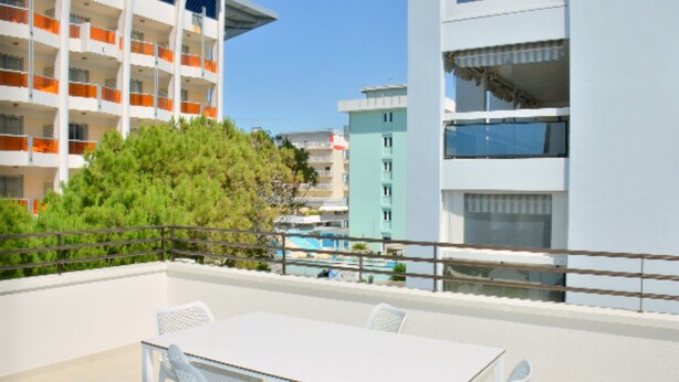 A balcony with a table and chairs, overlooking a pool and adjacent buildings. - Sunny and Bright Beautiful Apartment (San Michele al Tagliamento)