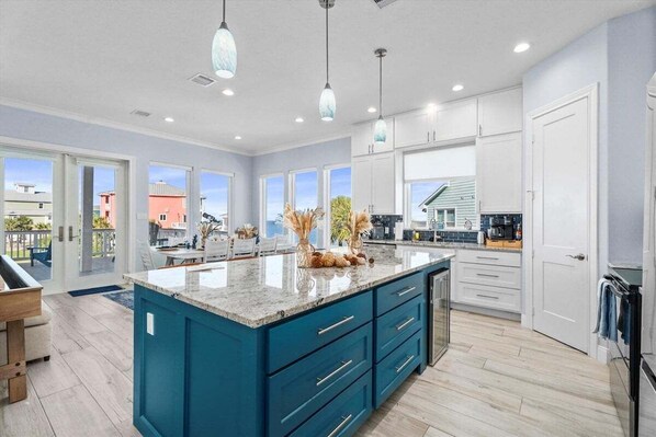 Una cocina moderna con una isla central grande, armarios blancos e iluminación colgante.