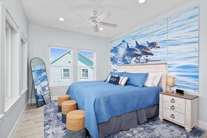 Un dormitorio con cama, mesita de noche, ventilador de techo y un amplio mural temático marino.