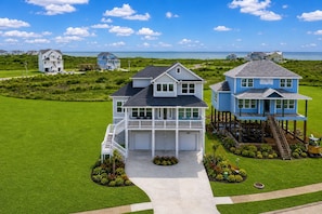 A large, two-story house with a balcony, a covered porch, and a view of the ocean.