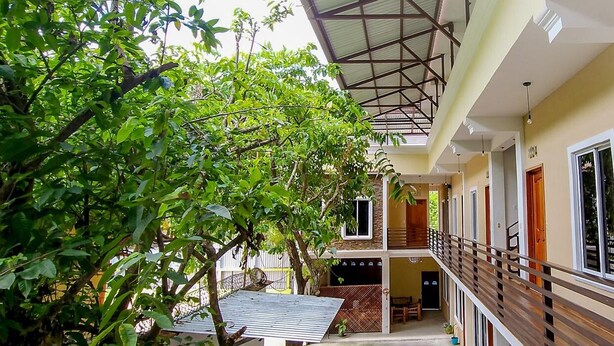 A covered outdoor corridor with a wooden railing, a staircase, and a view of a building with multiple doors and windows. - Hotel Maya Magic Petén (Flores)