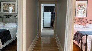 A narrow hallway with a bed on the left, a bed on the right, and a refrigerator in the background.