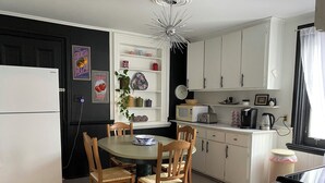 A compact kitchen with white cabinets, a dining table with chairs, a refrigerator, a microwave, a toaster, and a kettle.