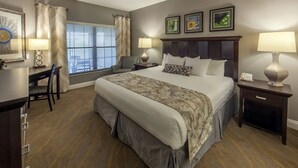 Habitación de hotel con una cama grande, dos mesitas de noche con lámparas, un escritorio con silla y una ventana con persianas.