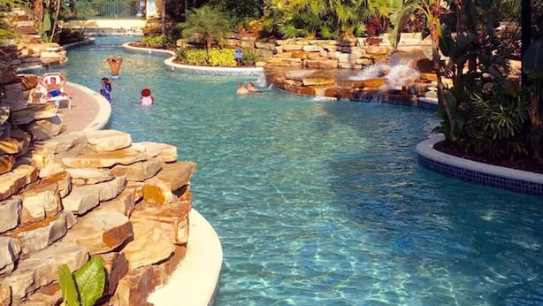 Una piscina con cascada, rodeada de rocas y plantas tropicales.