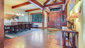 A dining area with wooden tables and chairs, a chandelier, and a large window with a view of trees.