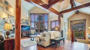 A spacious living room with wooden floors, a fireplace, a large window with a view, and a cozy seating area.