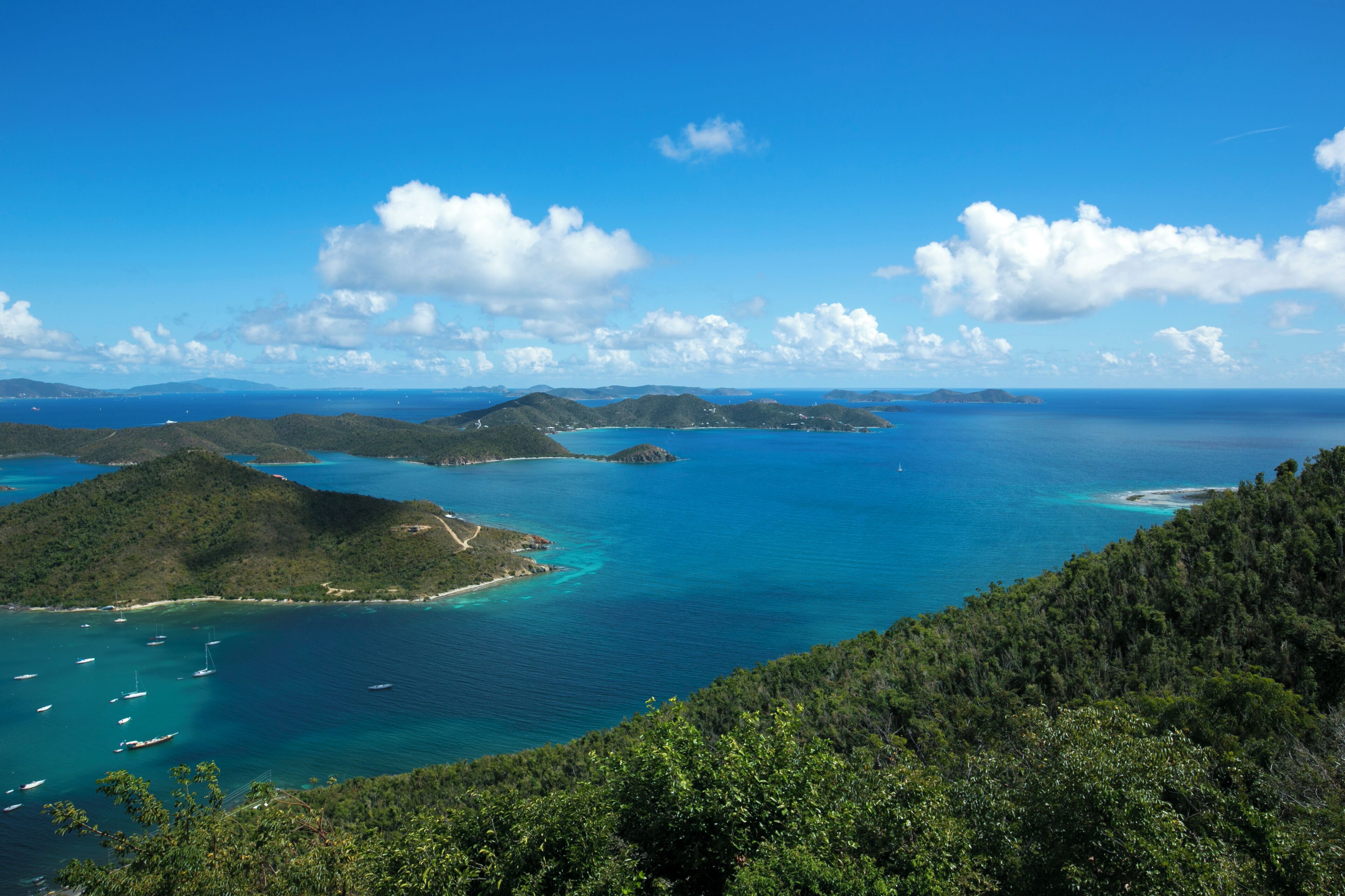 Un paysage côtier avec une eau d’un bleu limpide, des collines verdoyantes et quelques bateaux.