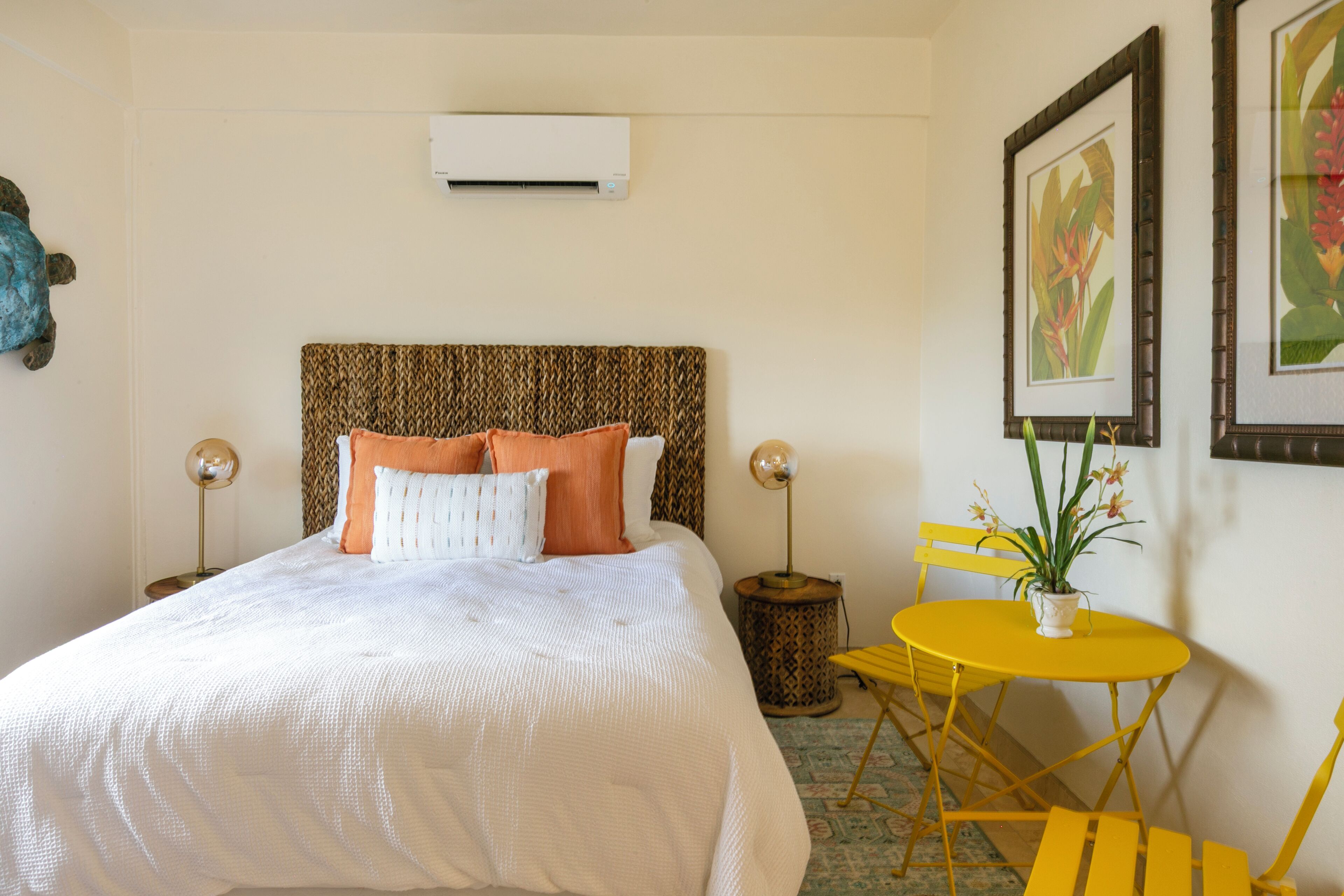 Una habitación de hotel con una cama, una mesita de noche, una lámpara, una pequeña mesa redonda con sillas y una planta en maceta.
