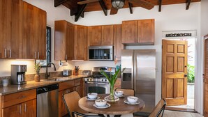 A kitchen with wooden cabinets, stainless steel appliances, a dining table with chairs, and a door leading outside. - Expansive Island Chain Views! Lunazul Cottage, 2BR/2BA, Solar Power Backup (Coral Bay)