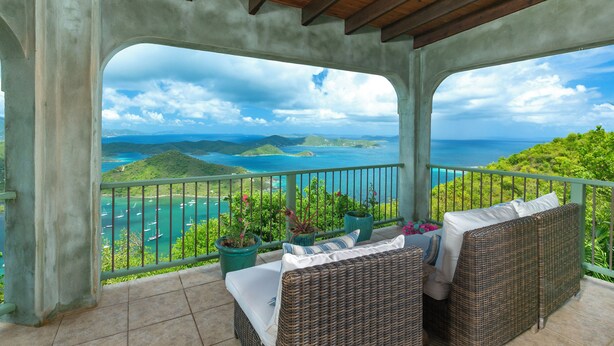 A covered balcony with wicker furniture, potted plants, and a view of the sea and hills. - Expansive Island Chain Views! Lunazul Cottage, 2BR/2BA, Solar Power Backup (Coral Bay)