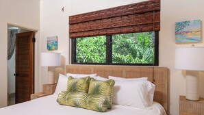 A neatly made bed with white and green pillows, a window with a view of greenery, and two bedside lamps. - Expansive Island Chain Views! Lunazul Cottage, 2BR/2BA, Solar Power Backup (Coral Bay)