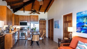 A kitchen with wooden cabinets, a dining table with chairs, a sofa, and a ceiling fan. - Expansive Island Chain Views! Lunazul Cottage, 2BR/2BA, Solar Power Backup (Coral Bay)