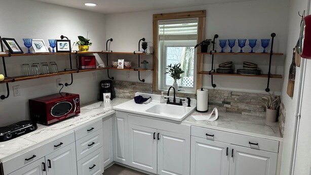A modern kitchen with white cabinets, a built-in oven, a sink, and a window with blinds.