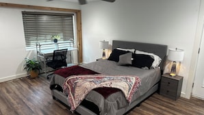 A bedroom with a bed, a desk, a chair, a ceiling fan, and a window with blinds.