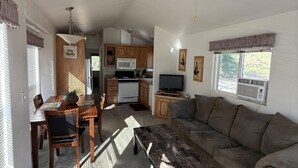 A spacious living room with a large sofa, a dining table with chairs, a kitchen area with wooden cabinets, a ceiling fan, and a television. - Cottage, Sleeps 4 - Scenic Cottage, 1 Bedroom, Sleeps 4 (Winters)