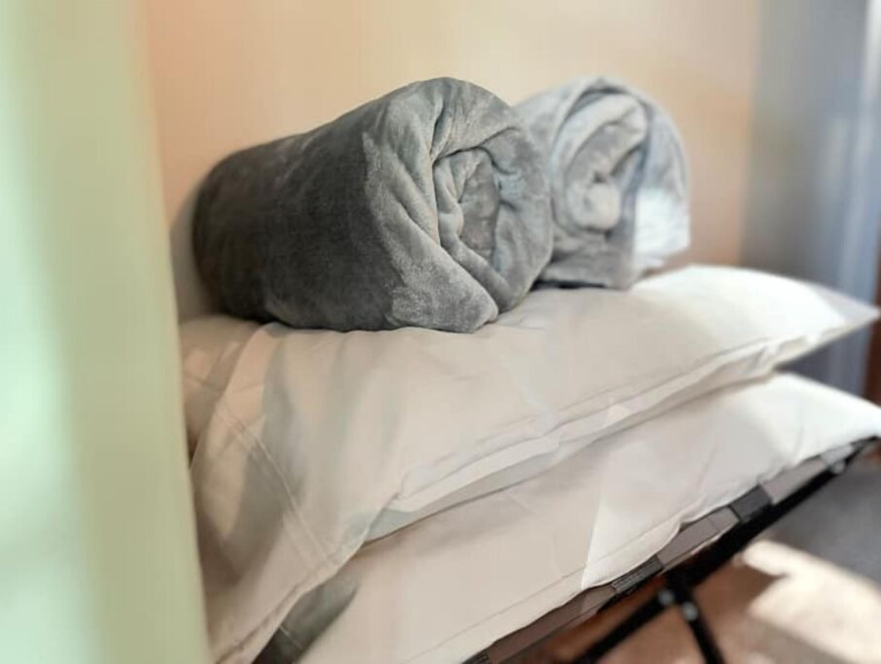 Una cama con un almohadón blanco y una manta gris.