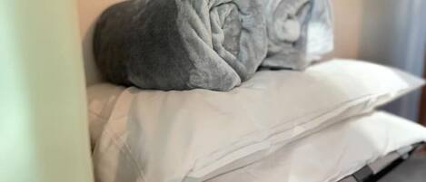 Una cama con un almohadón blanco y una manta gris.