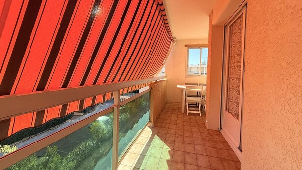 A balcony with a red-striped awning, a glass door, and a tiled floor. - C21Loctionvacances, T3 DUB- plages et commerces à pied (BORMES LES MIMOSAS)