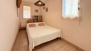 A bedroom with a bed, a bedside table, a lamp, a wardrobe, and a window with a curtain. - C21Loctionvacances, T3 DUB- plages et commerces à pied (BORMES LES MIMOSAS)