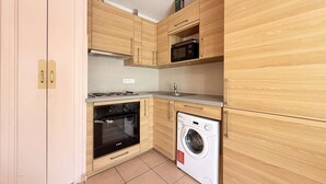 A compact kitchen with wooden cabinets, a microwave, an oven, and a washing machine. - C21Loctionvacances, T3 DUB- plages et commerces à pied (BORMES LES MIMOSAS)