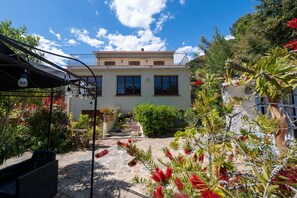 Un bâtiment à deux étages dot é d’un balcon, d’un chemin en pierre et de plantes en pot.