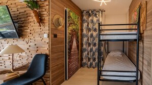 Ein kleines Zimmer mit Etagenbett, Schreibtisch mit Lampe, Stuhl, Wandfernseher und einer Tür mit dekorativem Gemälde.