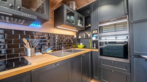 Eine moderne Küche mit dunklen Schränken, einer Holz Arbeitsplatte, einem eingebauten Backofen und einer Spritzschutzwand mit schwarzen Fliesen.