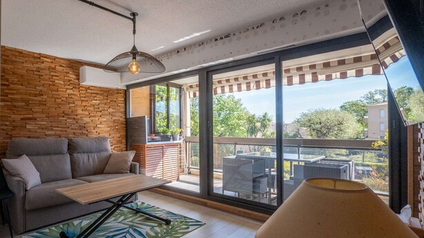 Ein modernes Wohnzimmer mit einer Couch, einem Couchtisch, einer Lampe und einer großen Schiebetür zum Außenbalkon mit Korbmöbeln.