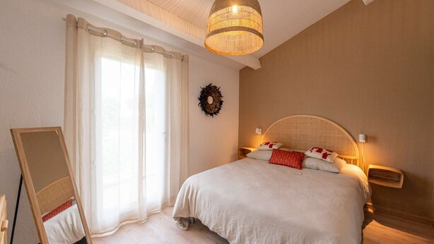 A bedroom with a large bed, a standing mirror, a wall-mounted light, and a ceiling light.